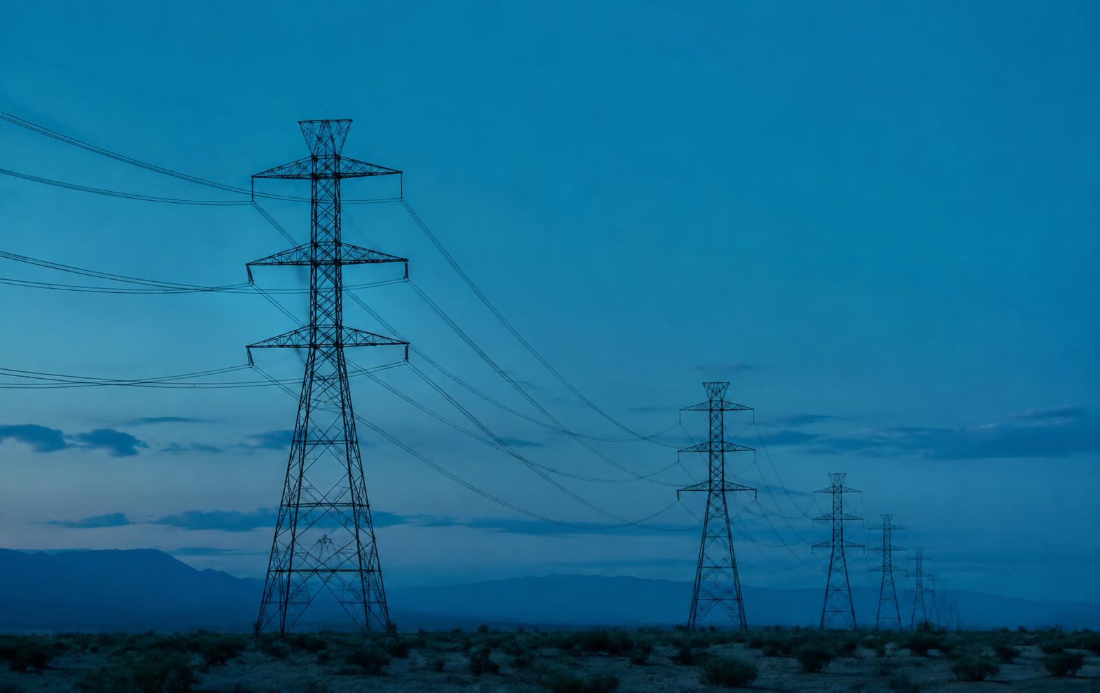 High-voltage transmission towers across a desert at blue hour